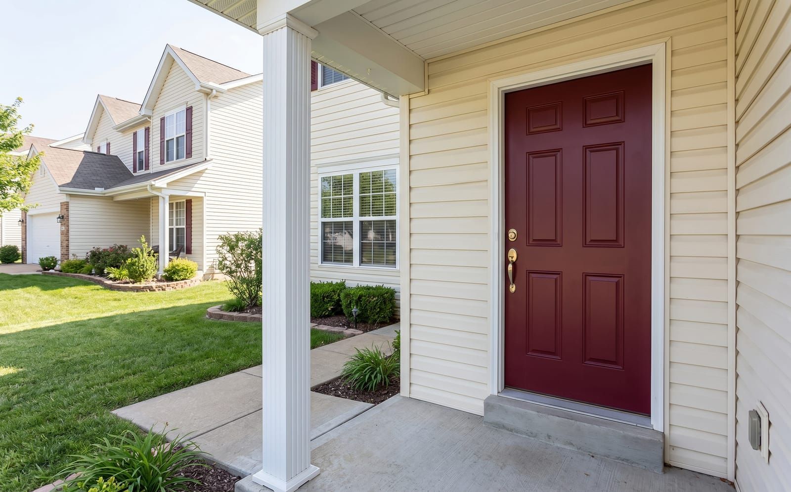 Burgundy red steel six-panel front entry door with brushed-brass handleset on a St. Peters cream vinyl-sided two-story home