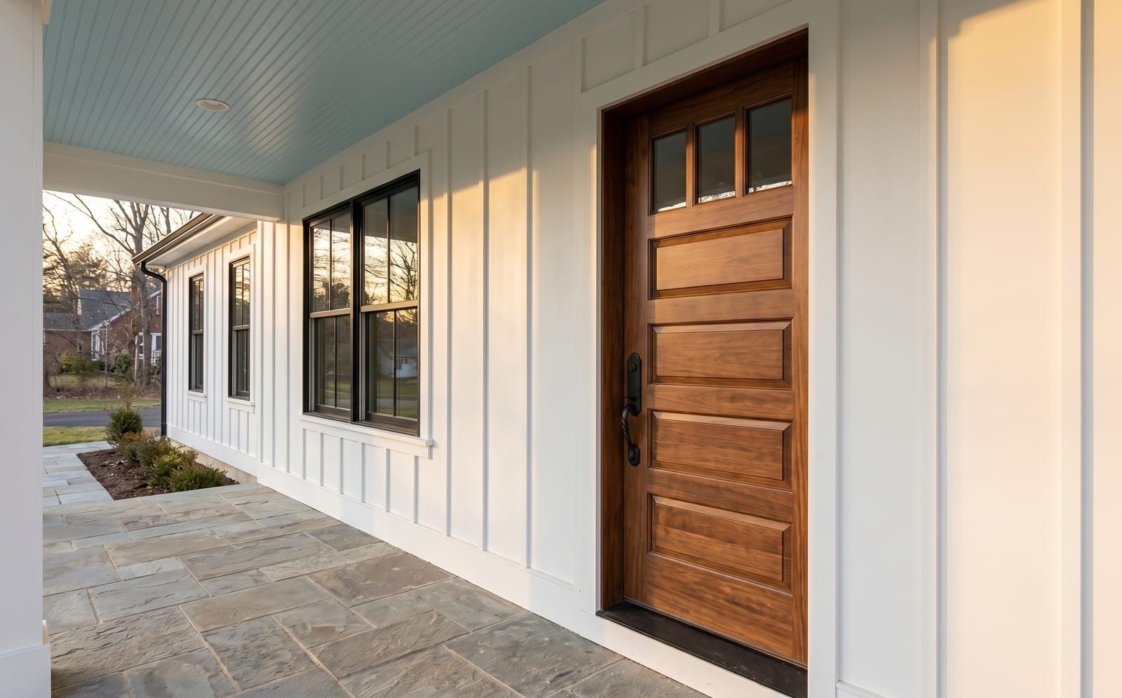 Walnut-stained craftsman five-panel solid wood front entry door with horizontal top lights and wrought-iron handleset on a Wentzville board-and-batten farmhouse