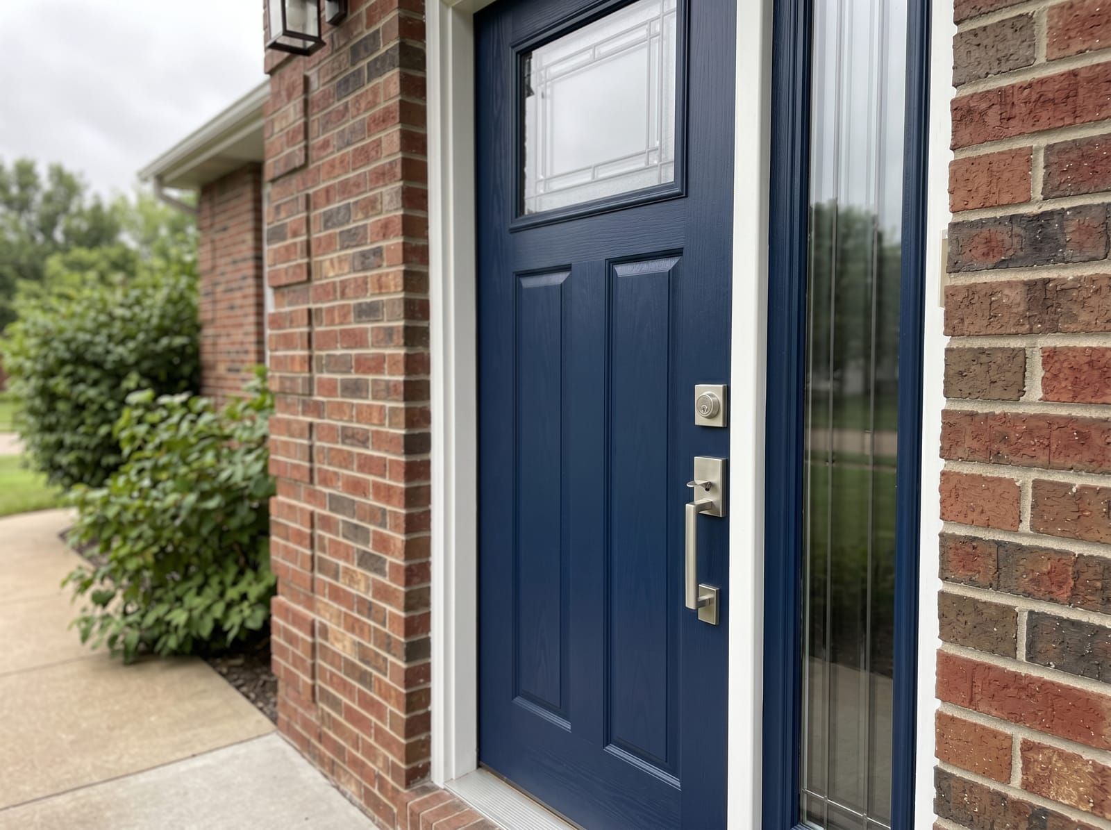 Navy fiberglass front entry door with single sidelight on a Saint Louis brick craftsman home