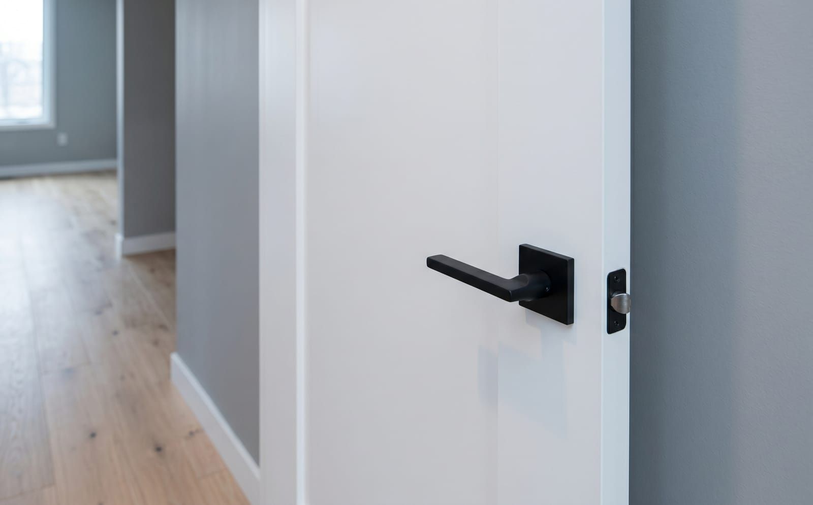 A modern flush-panel white interior door with a matte-black square lever handle in a contemporary trim-less opening