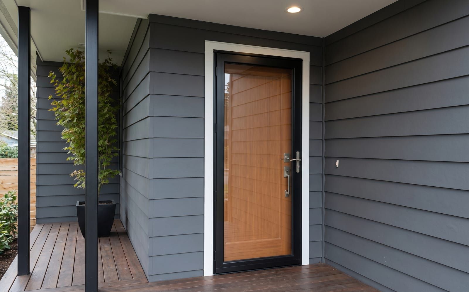 Black-frame full-view glass storm door installed over a natural-wood main entry door on a modern Hardie-board contemporary home in Saint Louis